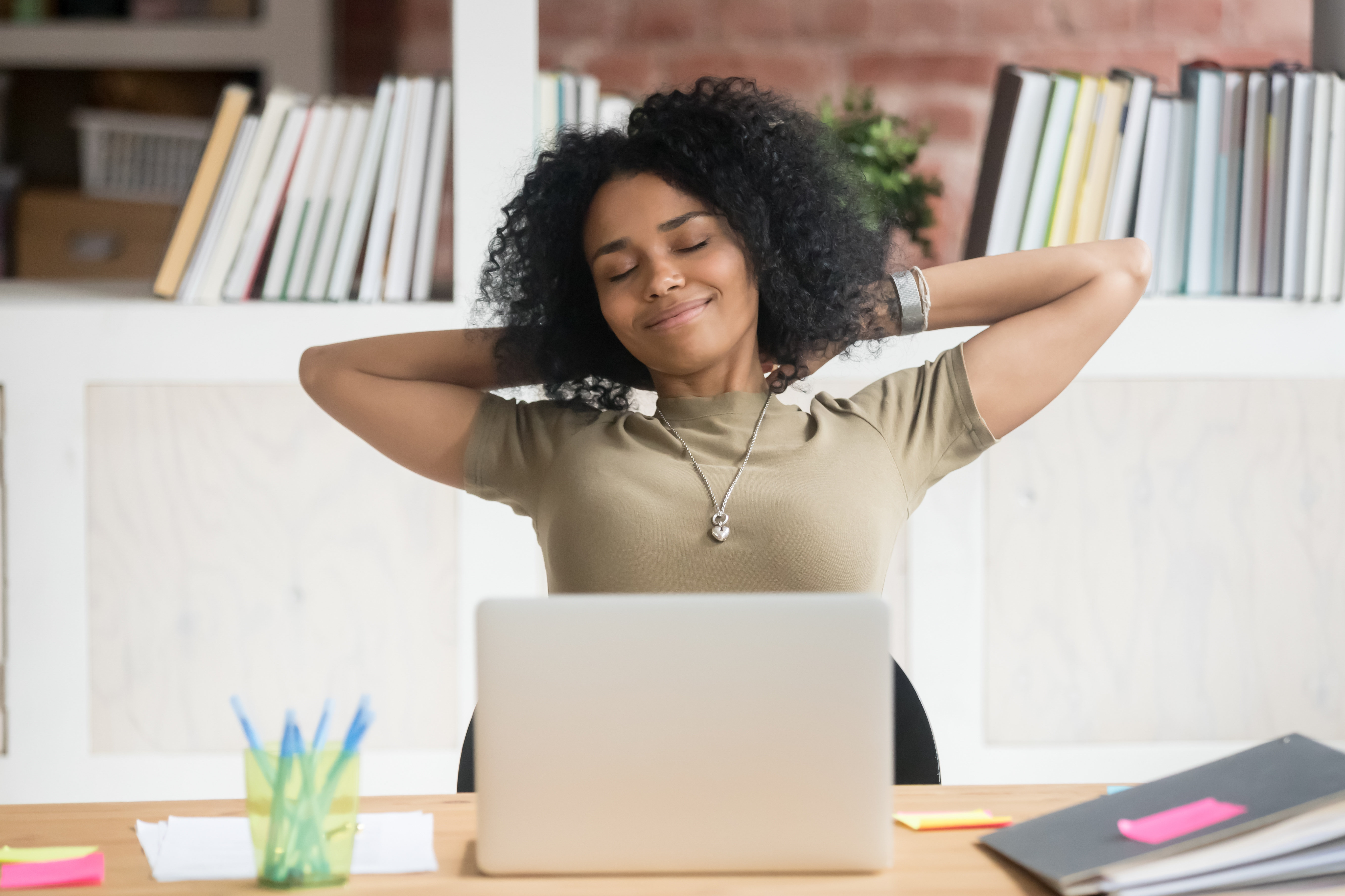 A woman stretches at her desk with a contented smile on her face.