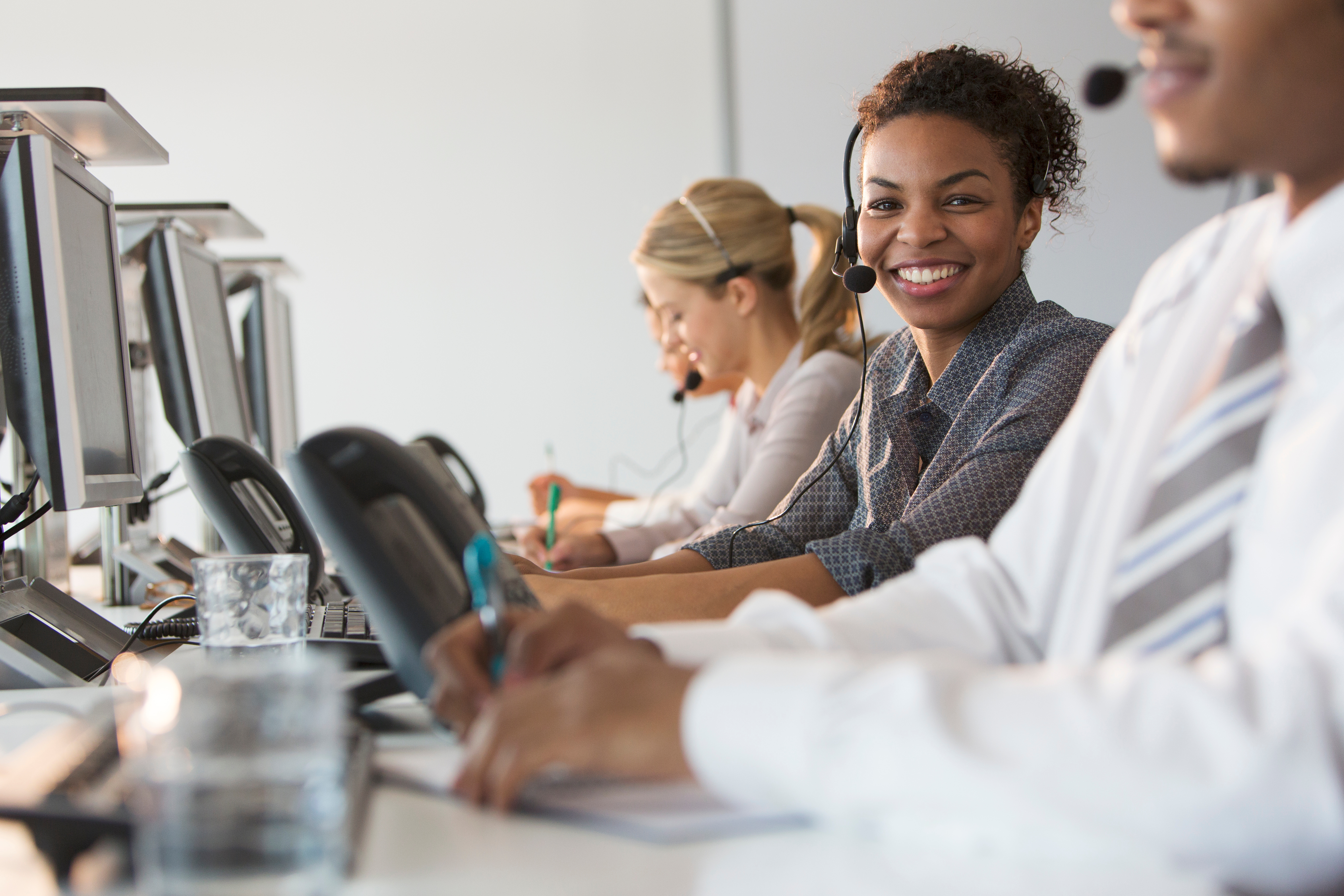 A smiling customer service representative sits in an outsourced call centre office.