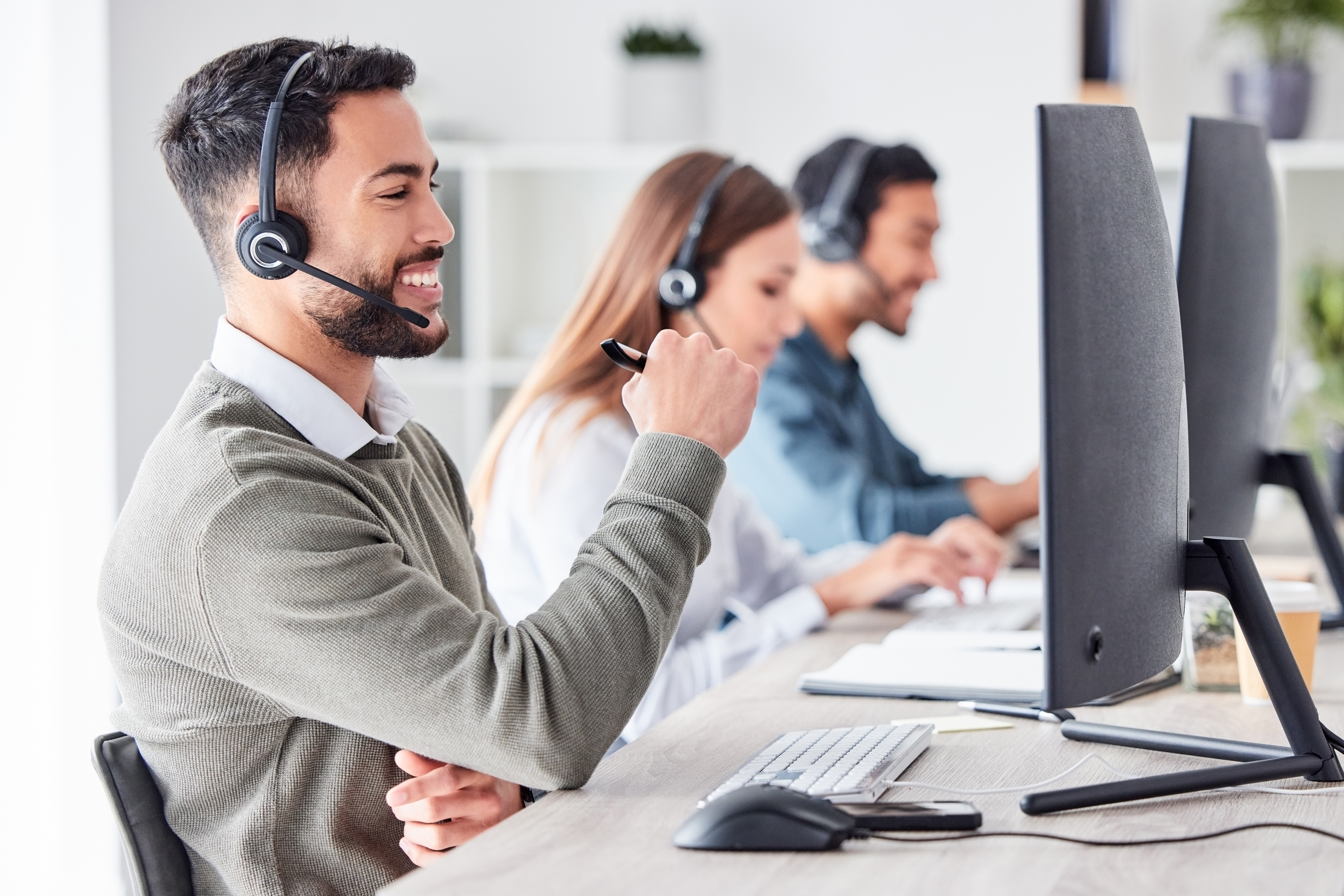 A man answers a customer call from his desk at a call centre.